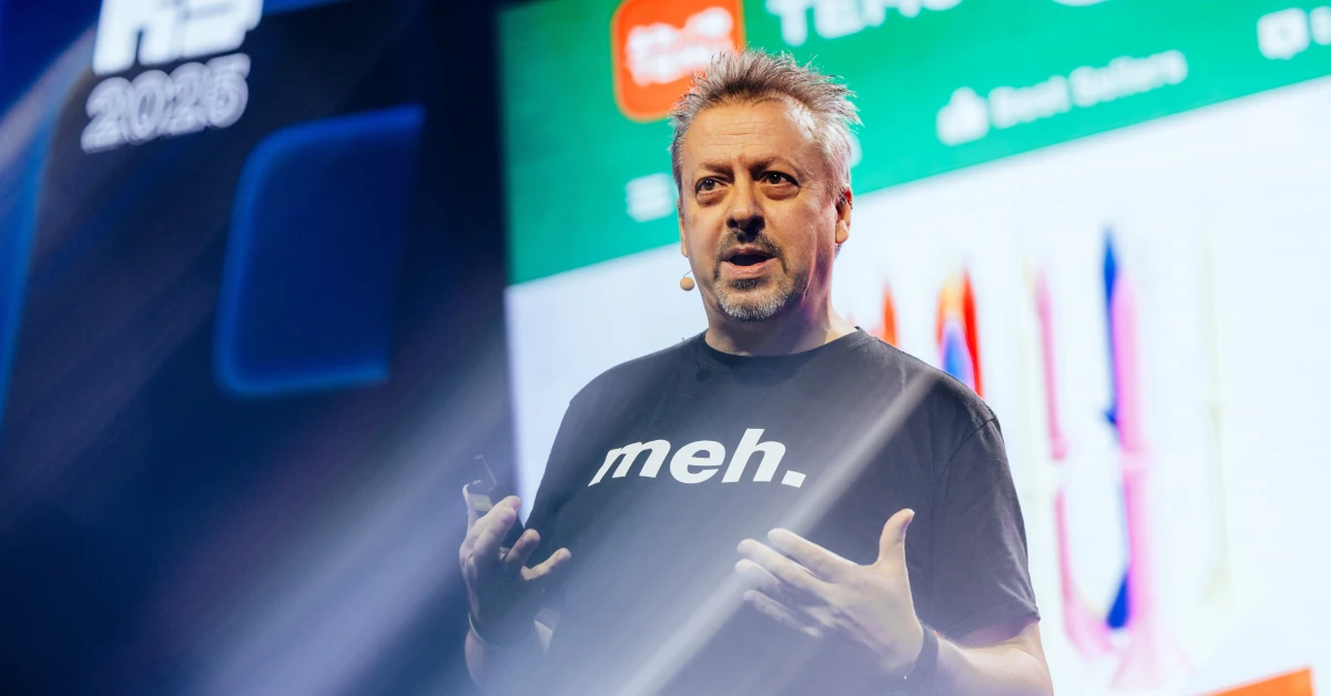 Ed Sander spricht auf der Bühne der K5 Konferenz. Er trägt ein schwarzes T-Shirt mit der Aufschrift "meh.", gestikuliert erklärend mit den Händen und blickt ins Publikum. Im Hintergrund ist eine leuchtende Präsentationsleinwand zu sehen.