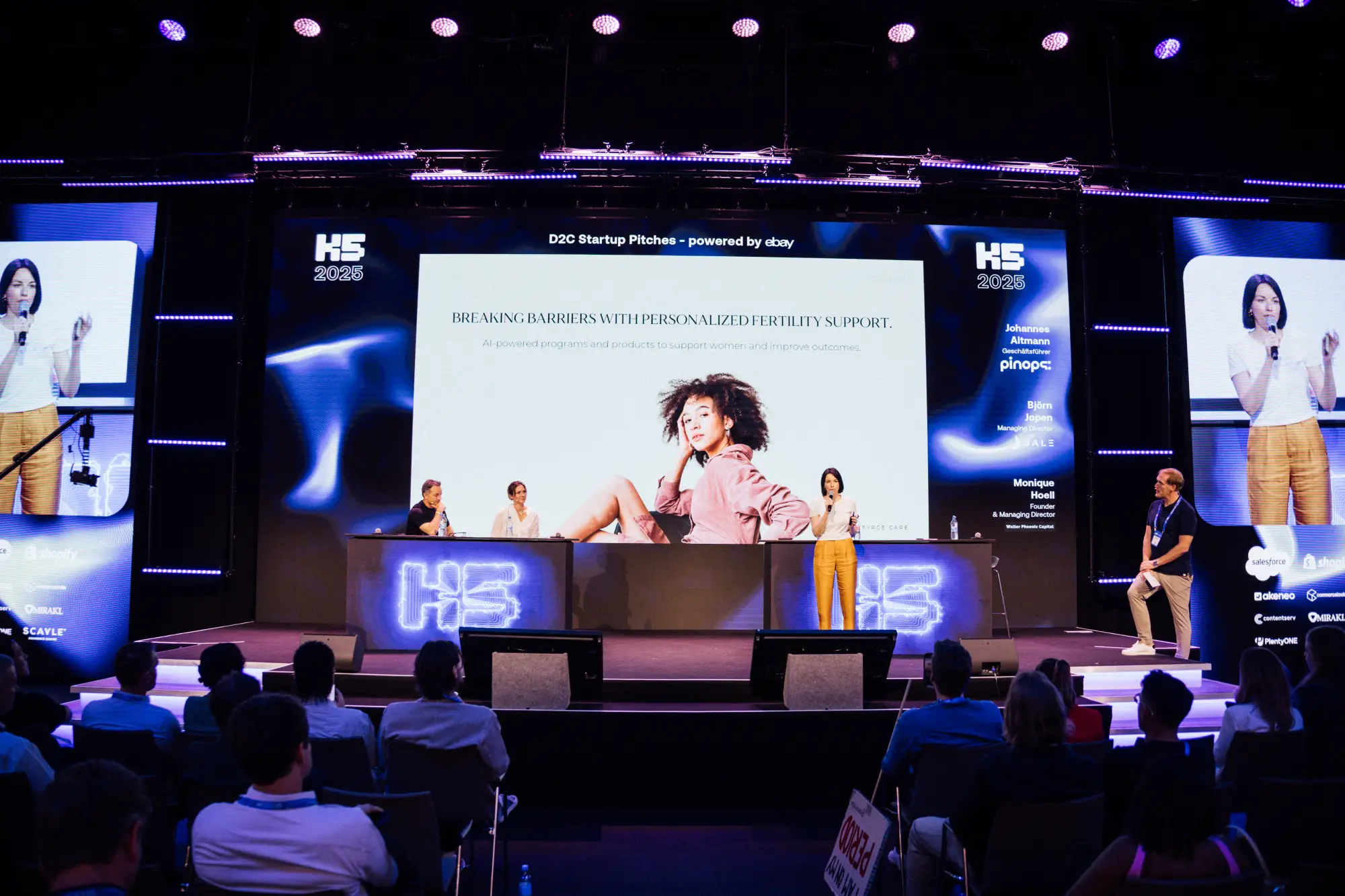 Eine Gründerin pitcht ihr D2C-Startup auf der großen Bühne der K5 Konferenz. Im Hintergrund zeigt eine riesige LED-Leinwand ihre Präsentation zum Thema 
