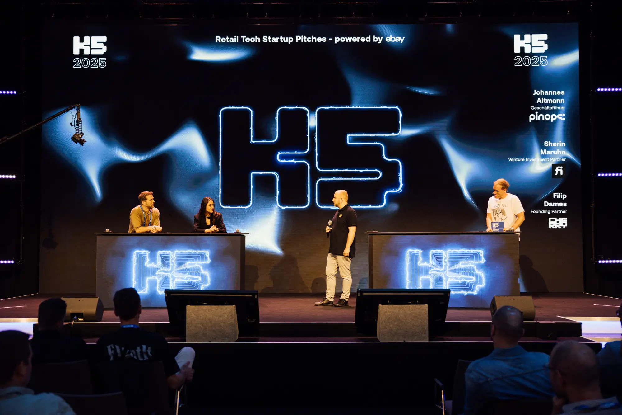 Ein Gründer steht mit einem Mikrofon auf der großen Bühne der K5 Konferenz und pitcht sein B2B-Geschäftsmodell. Im Hintergrund leuchtet eine gigantische LED-Wand mit dem K5-Logo und dem Titel 
